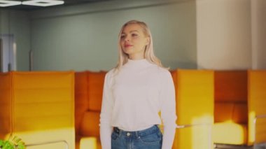 Modern ofis çalışma alanında açık renk saçlı, gülümseyen beyaz kız. Kadın ofis müdürünün portresi etrafa bakıyor ve sonra iyi bir ruh hali içinde kameraya bakıyor. Gerçek insanlar dizisi