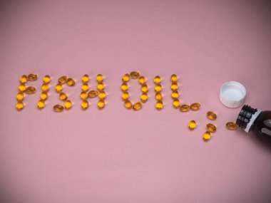 Balık yağı harfleri pembe arka planda balık yağı kapsülleriyle kaplı. Sağlık ve sağlıklı yaşam tarzı kavramı.