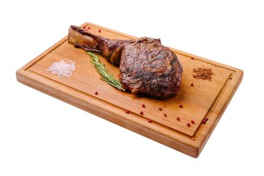 Mükemmel pişirilmiş pirzola bifteği, otlar ve baharatlarla süslenmiş ahşap bir kesme tahtasının üzerinde duruyor. Kaba tuz ve baharatlar sunuma lezzetli bir yemeğe hazır..