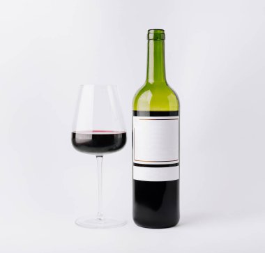 Zengin kırmızı şarap, parlak bir şarap şişesinin yanındaki bardağa dökülüyor. Ortam minimalist, şarabın güzelliğini vurguluyor, odaklanmak için beyaz bir arka planı var..