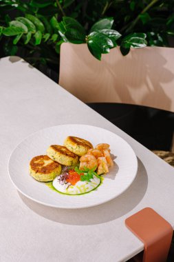 Bu yemekte lezzetli karideslerle eşleştirilmiş altın-kahverengi deniz ürünleri kekleri yer alıyor. Beyaz bir tabakta sanatsal olarak düzenlenmiştir, taze yeşillikler ve canlı süslerle çevrelenmiştir..