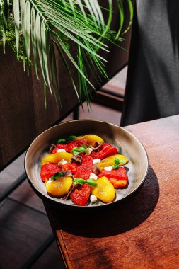 Ahşap bir masada kırmızı ve sarı biber dilimleri içeren parlak renkli sebze salatası. Taze yeşillik ortama canlı bir dokunuş katıyor. Sağlıklı bir atıştırmalık için mükemmel.