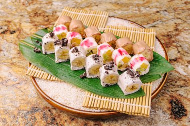 Çok güzel düzenlenmiş suşi tabağı. Meyvelerle dolu, yaratıcı malzemelerle dolu canlı rulo sergiler. Sunum lezzet ve renklerin sanatsal karışımını vurgular.
