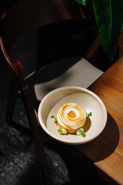 Süs olarak taze nane yaprakları olan yuvarlak bir tabakta güzel düzenlenmiş bir tatlı bulunur. Kurulumda bir ahşap masa ve yakındaki bitkilerden gelen yeşillik dokunuşu yer alıyor..