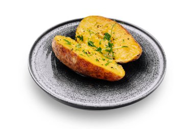 Fırında patates ikiye ayrılır ve siyah benekli bir tabağa yerleştirilir. Bitkiler ve baharatlarla kaplı, basit ama çekici bir yemek sergileniyor. İçindeki patates sarı ve yumuşacık..