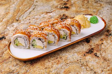 Suşi dürümleri beyaz bir tabakta, avokado, tavuk ve susam soslu. Zencefil ve wasabi, yeni bir lezzet deneyimi için yanına yerleştirilir..