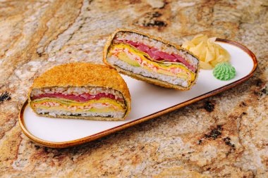 Canlı bir katsu sandviçi yarım tabaka pirinç katmanları, pişirilmiş etler ve dekoratif bir tabakta renkli sebzeler. Tabakta yeşil wasabi ve yanında zencefil turşusu var..