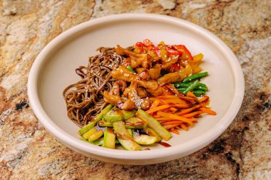 Renkli bir soba erişte kasesinde ızgara tavuk, kabak, havuç ve dolma biber gibi taze sebzeler yer alır. Yemek mermer bir masada ustalıkla hazırlandı, tadını çıkarmaya hazır..