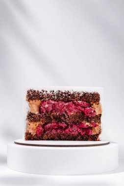 Çok güzel hazırlanmış bir tatlı, beyaz bir kaide üzerinde çarpıcı bir sunumla birden fazla pasta, krema ve meyve katmanı sergiler. Canlı renkler zengin bir tadı işaret ediyor..