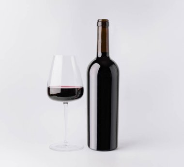 Bir şişe kırmızı şarap, kısmen koyu kırmızı sıvıyla dolu berrak bir bardağın yanında duruyor. Her iki öge de temiz beyaz bir arkaplanda, basit ve zarif bir sahne yaratıyor..
