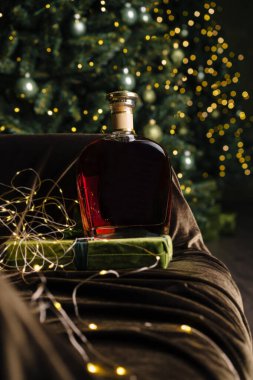 Güzel tasarlanmış bir viski şişesi yumuşak bir kanepede yeşil paketlenmiş bir hediyenin yanında oturur. Yakındaki bir Noel ağacından gelen parıldayan ışıklar sıcak ve davetkar bir atmosfer yaratır..