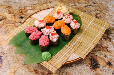 Canlı bir tabakta tonbalığı, yengeç ve renkli süslemelerle süslenmiş somon da dahil olmak üzere çeşitli suşi çeşitleri sergilenmektedir. Suşi düzgün bir şekilde bambu hasırının üzerine dizilmiştir..