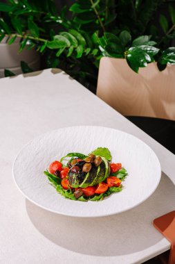 Güzelce hazırlanmış bir ızgara avokado salatasında beyaz bir tabakta taze kiraz domatesleri ve fındıklar bulunur. Bu renkli yemek modern bir restoranda sağlıklı bir öğle yemeği için mükemmel..