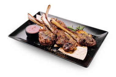 Sulu kuzu pirzolası ustalıkla ızgara yapılır ve siyah bir tabakta düzenlenir. Lezzetli yemeğe lezzet katmak için küçük bir kase sos eşlik eder..