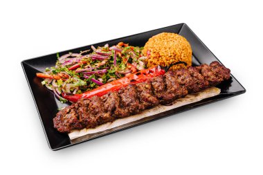 Bir tabak ızgara kebap yumuşak et şişleri, canlı pilav ve domatesli renkli bir salata, soğan ve bitkiler içerir. Bu yemek iştah açıcı görünüyor ve çeşitli tatlar sunuyor..