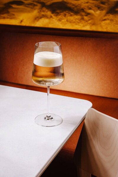 A clear glass filled with sparkling drink sits on a smooth, white marble table. The warm background features soft lighting that enhances the inviting atmosphere.