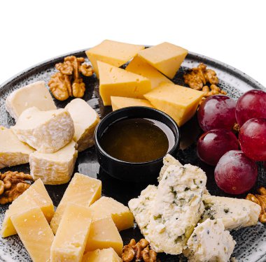 Renkli bir peynir tabağında çeşitli peynir türleri, taze üzümler, cevizler ve bir kase bal bulunur. Bu düzen, sosyal etkinlikler ya da takılma yerleri sırasında misafirleri eğlendirmek için mükemmel..