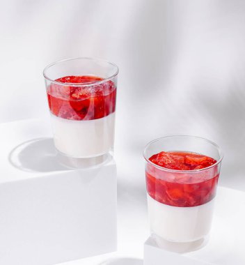 İki temiz fincanda taze çilek ve kırmızı jöle katmanlı kremalı bir tatlı var. Pürüzsüz beyaz taban, canlı üstüyle çok güzel zıtlaşıyor ve davetkar bir ikram oluşturuyor..