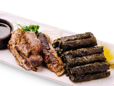 Lezzetli ızgara et, güzelce sarılmış asma yapraklarının yanında duruyor. Küçük bir kase sos ve taze limon bu iştah açıcı yemeğe lezzet katar, doyurucu bir yemek ya da özel bir gün için mükemmeldir..