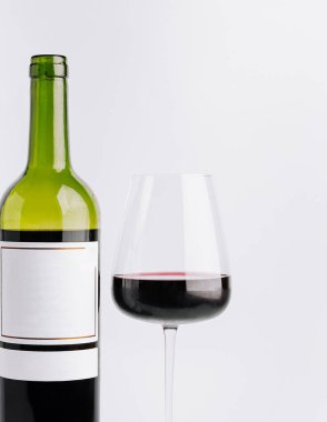 Yeşil bir şişe kırmızı şarap, koyu kırmızı şarapla dolu berrak bir bardağın yanında duruyor. Zengin rengini beyaz arka planda sergiliyor. Tatma etkinliği ya da kutlama için mükemmel..