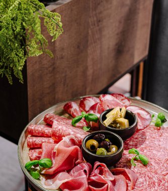 A beautifully arranged platter displays various cured meats, olives, and artichokes. Fresh herbs add color, creating an appetizing and inviting presentation for sharing or snacking.