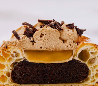 Cazip bir tatlı, üzerinde zengin çikolata tabakaları, kremalı dolgu maddeleri ve çikolata parçacıkları sergiler. Bu enfes ikram, sıcak bir pastane ortamında hoşgörüye davet ediyor..