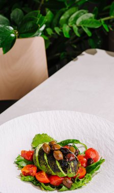 Bu gurme tabağında domates ve yeşillikler de dahil olmak üzere sebzelerin minimalist beyaz bir tabakta sanatsal bir şekilde sunulduğu yaratıcı bir düzenleme sergilenmektedir..