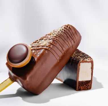 İki çikolata kaplı dondurma sergileniyor. Bir çubuk parlak bir yüzey ve yuvarlak bir kaplama ile bütündür, diğeri ise kremsi içini gösterir. İkisi de zengin ve cazip görünüyor..