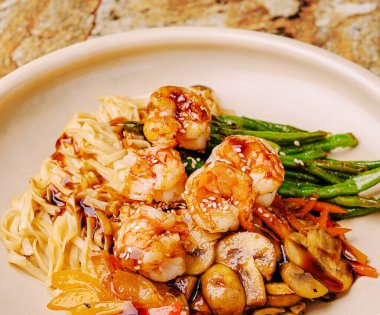 Yumuşak karides, renkli sebzeler ve yumuşak erişte içeren lezzetli bir kızartma. Yemek susam tohumlarıyla süslenmiş, bu da onu görsel olarak çekici bir yemek yapıyor..