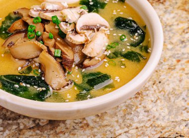 Lezzetli bir kase miso çorbası granit bir masada duruyor. Çorba dilimlenmiş mantar, yeşil soğan ve deniz yosunu içeriyor. Serin bir günde rahatlatıcı bir yemek yaratıyor..