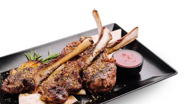 Sulu ızgara kuzu pirzolası siyah bir tabakta güzelce düzenlenmiştir. Tabakta bol bir sos ve garnitür için taze otlar var. Bu da onu cazip bir yemek yapıyor..