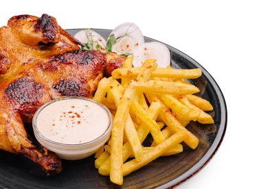 Sulu ızgara tavuk, yanında altın çıtır patates kızartması ve küçük bir kase kremalı sosla birlikte siyah bir tabakta duruyor. Tat vermesi için biraz sebze turşusu eklenir..