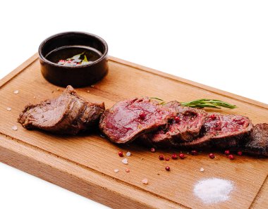 Küçük bir kase sos ve taze otlarla birlikte sulu et dilimleri ahşap bir tahtada güzelce düzenlenir. Sunumda tazelik ve lezzet vurgulanıyor.