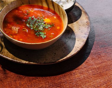 Sıcak bir kase zengin çorba bir kase kremalı sosun yanında dokulu bir tabağın üzerinde oturur. Taze otlar tabağı süslüyor, canlı renkler ve davetkar aromalar sergiliyor..