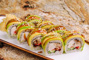 Sekiz renkli suşi rulosu bir tabakta güzelce sıralanır. Her rulo avokadoyla kaplanmış ve üzerine zencefil turşusu serpiştirilmiş sos serpiştirilmiş..