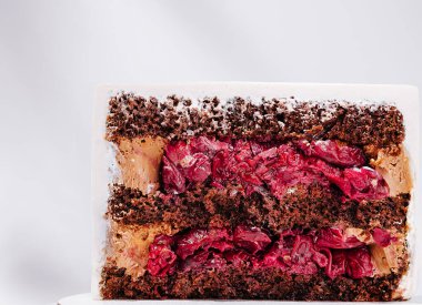 Bu tatlı, turta dilimleri ve kremayla dolu zengin çikolata katmanlarına sahiptir. Pasta güzel bir şekilde sergileniyor, nemli dokusu ve canlı renkleri vurgulanıyor..