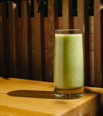 Uzun, canlı, yeşil bir bardak meyve püresi tahta bir masada duruyor..