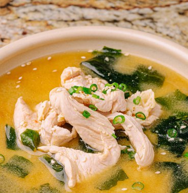 Sıcak tavuk çorbalarıyla dolu bir kase taze tavuk dilimleri ve taze yosun. Yeşil soğan serpilmiş, bu rahatlatıcı yemek sunar..