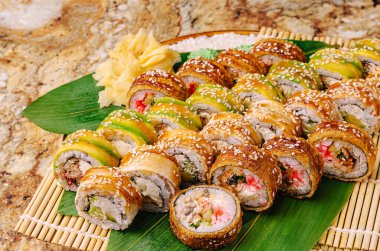 Muz yaprakları üzerinde rengarenk bir suşi rulosu çeşidi düzenlenir. Yeşil ve altın maki börekleri, zencefil ve susam tohumlarıyla süslenmiş yengeç ve sebze dolgusunun yanında otururlar..