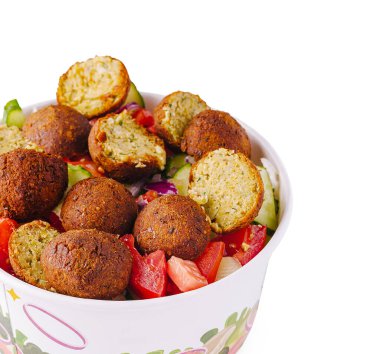 Domates ve salatalık gibi taze sebze karışımının tepesinde gevrek falafel toplarıyla dolu renkli bir kase. Sahne, öğle yemeği ya da atıştırmalık için sağlıklı bir yemek seçeneği öneriyor..