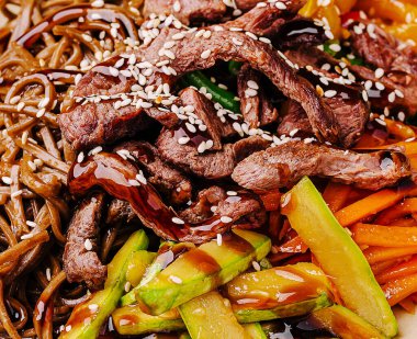 Sulu sığır eti şeritleri rengarenk sebzelerle kızartılır ve erişte üzerine servis edilir. Susam tohumlarıyla süslenmiş bu yemek lezzetli ve besleyici bir yemektir..