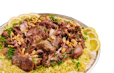 Canlı bir tabakta yumuşak pirinçle servis edilen yumuşak kuzu eti, üzerinde çıtır fındık ve taze limon dilimleri bulunuyor. Bu yemek lezzet ve dokuların zengin bir kombinasyonunu vurgular.