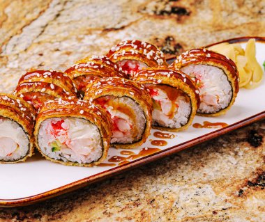 Yengeç etinden yapılmış lezzetli suşi ruloları ve susamlı kaplamalar çekici bir şekilde kaplanmıştır. Ekmekler ahşap bir tabakta zencefilli, canlı renkler ve dokularla servis ediliyor..