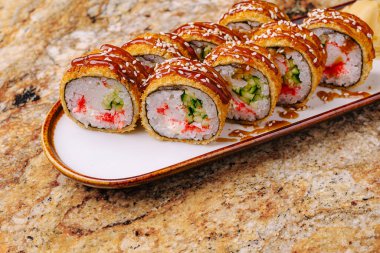 Bir tabakta çıtır çıtır bir tabakla kaplanmış ve tatlı sosla ıslanmış suşi ruloları var. Suşi, yengeç, salatalık ve pirinç gibi renkli dolguları içerir..