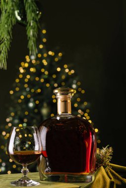 Kehribar içeceğiyle dolu bir bardağın yanındaki masaya zengin bir şişe viski konur. Yumuşak sarı ışıklar yakındaki bir Noel ağacında parıldıyor, sıcak atmosferi güçlendiriyor..