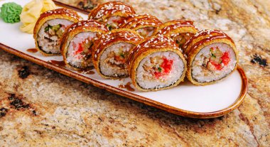 Lezzetli suşi ruloları, çıtır tempura ve renkli dolgular içeren uzun bir tabakta dikkatlice düzenlenir. Wasabi garnitürleri ve turşulu zencefil. Hoş bir dokunuş..