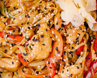 Susam tohumlarıyla kaplı taze tavuk ve çeşitli sebzelerle karıştırılmış canlı bir şehriye karışımı bir kasede servis edilir. Keyfini çıkarmaya hazır lezzetli bir yemek..