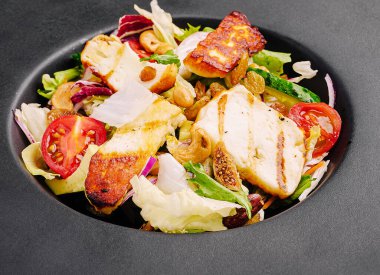 Renkli bir salatada modern siyah bir kâsede pişirilmiş ızgara tavuk, taze marul, domates ve fındık bulunur. Yemekler canlı malzemeler sergiliyor. Görsel olarak çekici ve sağlıklı..