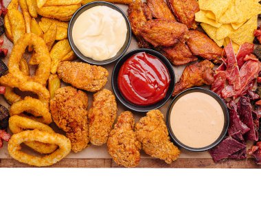 Renkli bir kızarmış tavuk kanadı, soğan halkaları, nachos ve çeşitli soslar ahşap bir tahtanın üzerinde sergilenmektedir. Sıradan bir toplantıyı ya da kutlamayı paylaşmak için mükemmel..