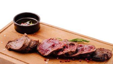 Yavaş pişirilmiş et dilimleri ahşap bir tahta üzerinde düzenlenir. Küçük bir kase sos, zengin lezzetleri artırmak için yemeğe eşlik eder. Süslenmek için taze bitkiler konur..